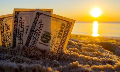 Three 100 dollar bills are buried in sand on the beach near sea at sunset. Offshore trust concept.