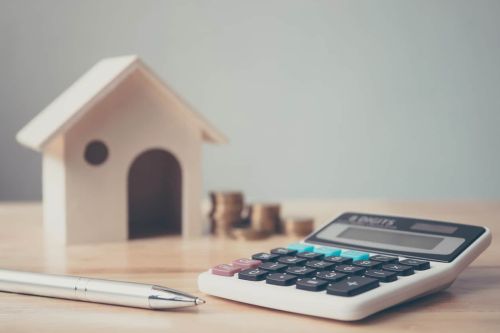 Calculator with wooden house and coins stack and pen on wood table. Property investment and house mortgage. Concept for How to Transfer Property into a Trust.