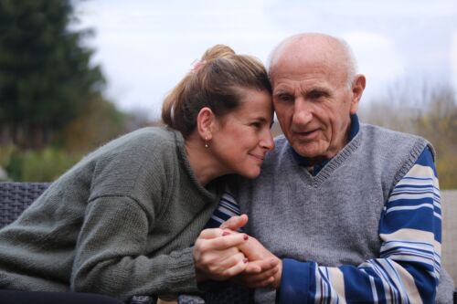 Elderly father and daughter sitting side by side in the garden and lovingly holding hands. Image is a concept for a blog discussing the importance of a power of attorney for elderly parent.