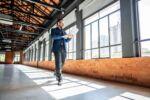 Mature businessman walking and using laptop at empty office for sell at real estate visual concept for a blog discussing commercial real estate outlook and trends.